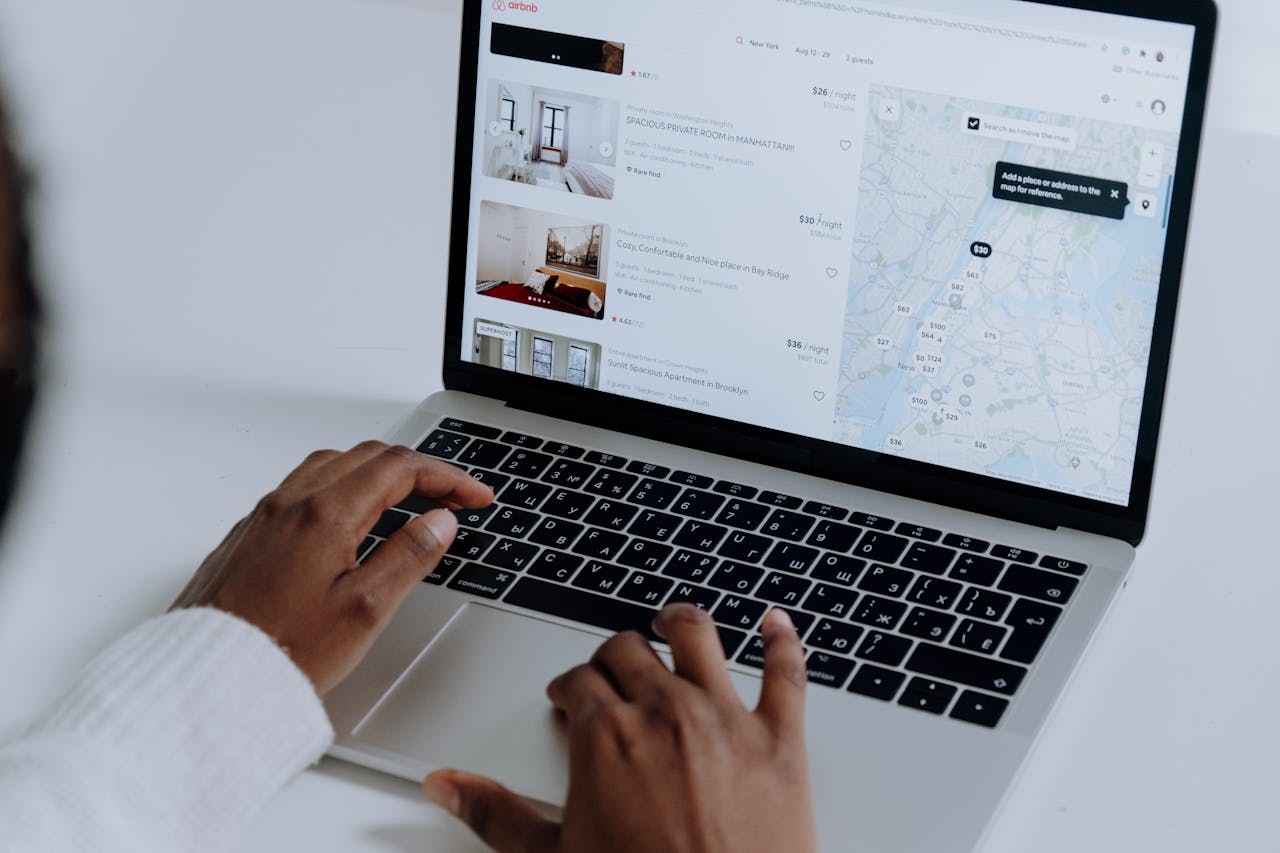 about-us Hands typing on laptop searching Airbnb for accommodation options with map view.